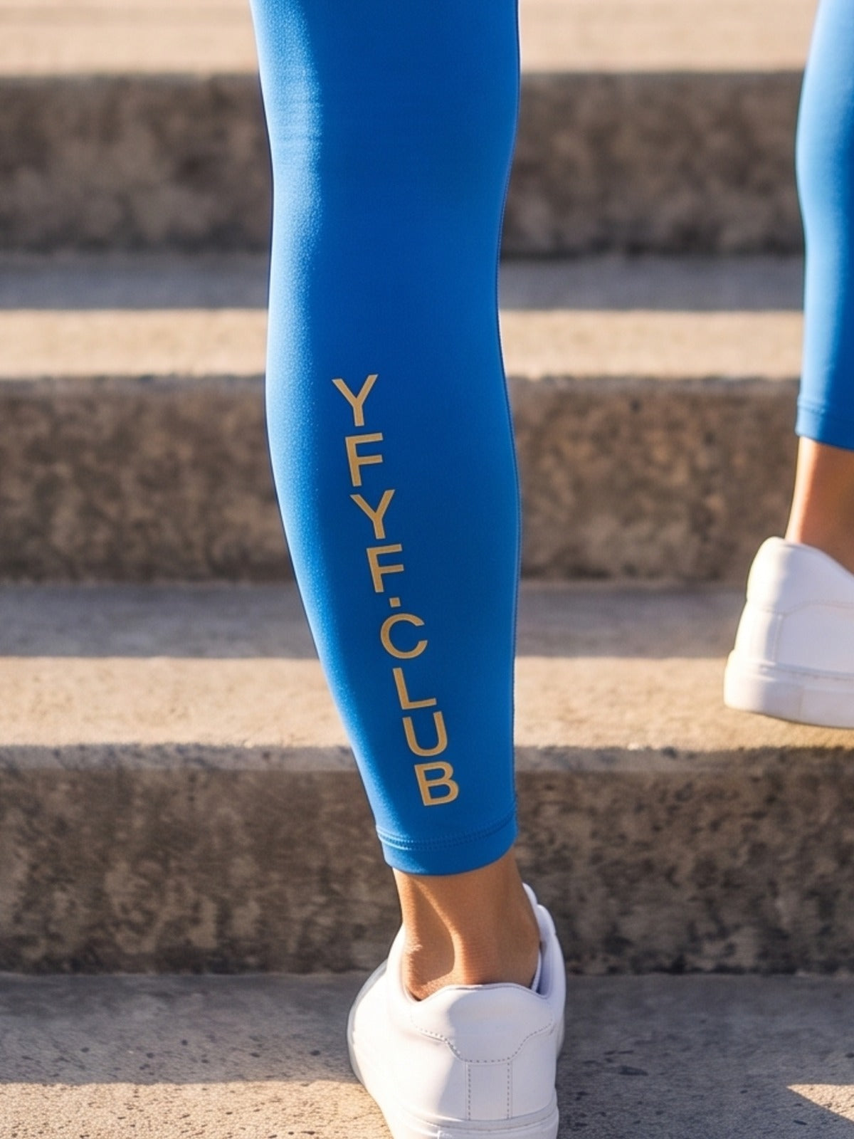 Close-up of gold YFYF.CLUB printed on the calf of the Coastal Blue Gold Logo leggings