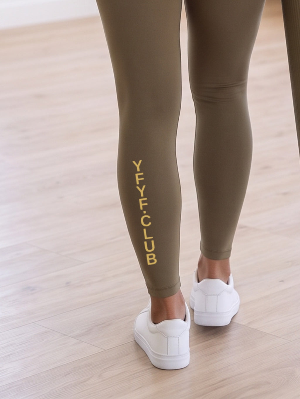 Close-up of gold YFYF.CLUB printed on the calf of the Olive Gold Logo leggings