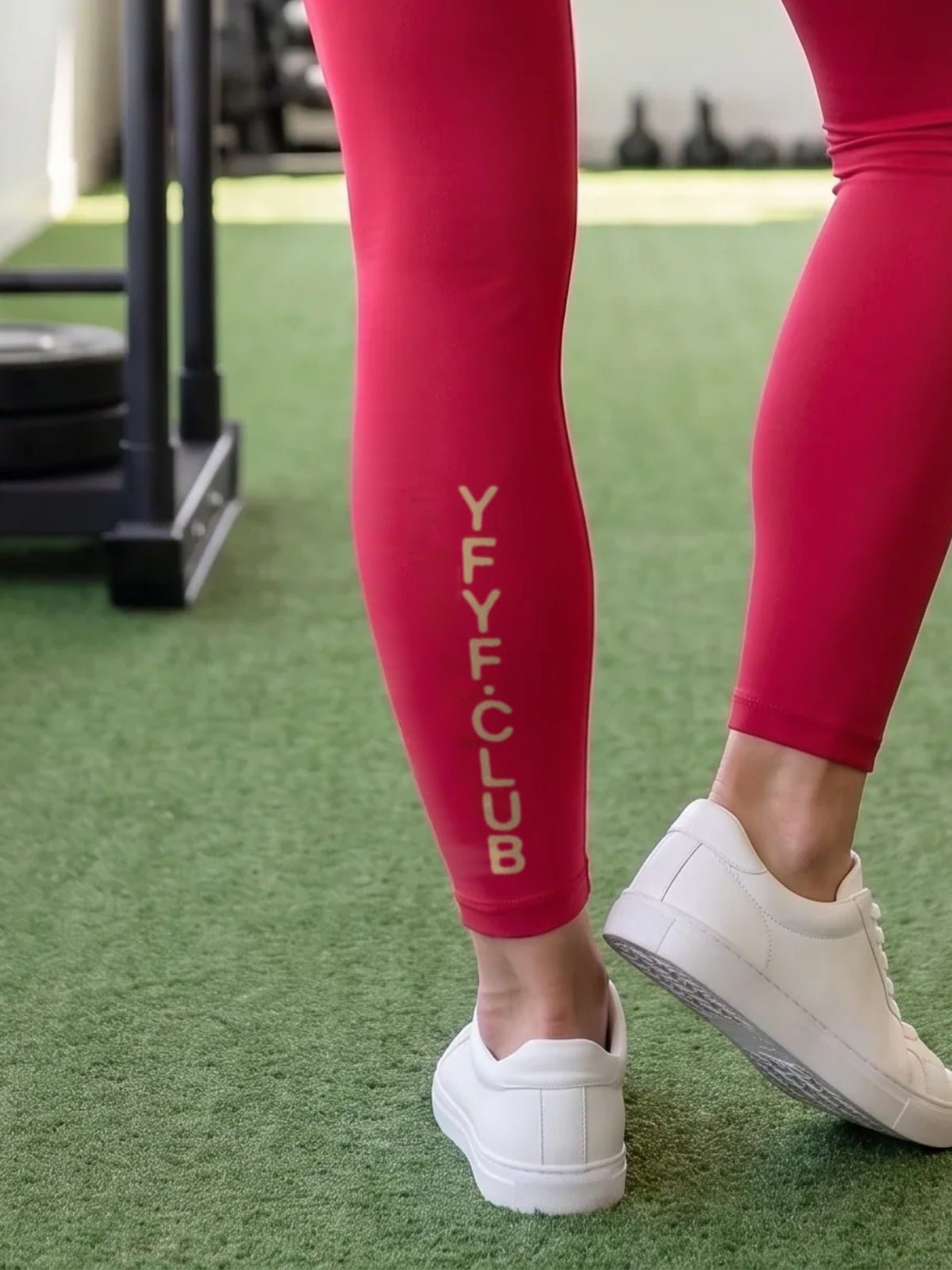 Close-up of gold YFYF.CLUB printed on the calf of the Cherry Gold Logo leggings